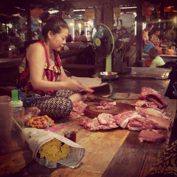 Woman chopping meat with a cleaver.